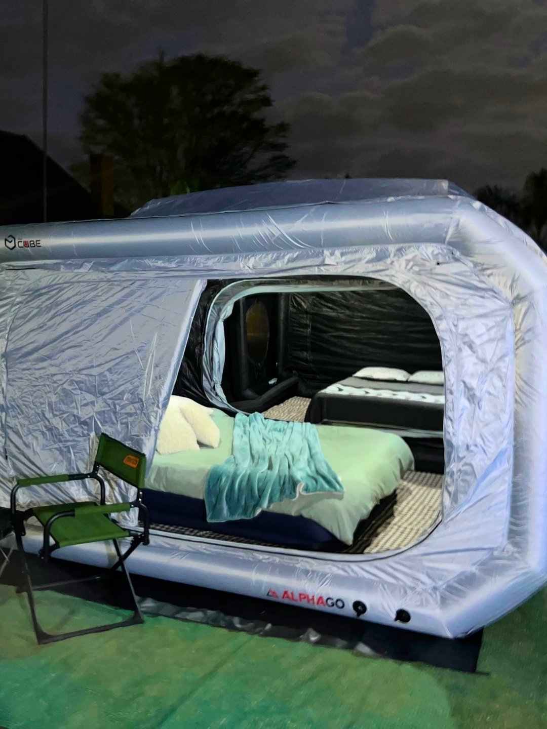 Close view of the Wander Cube Starlight doorway at night with a bed made up in green linen and a camp chair outside