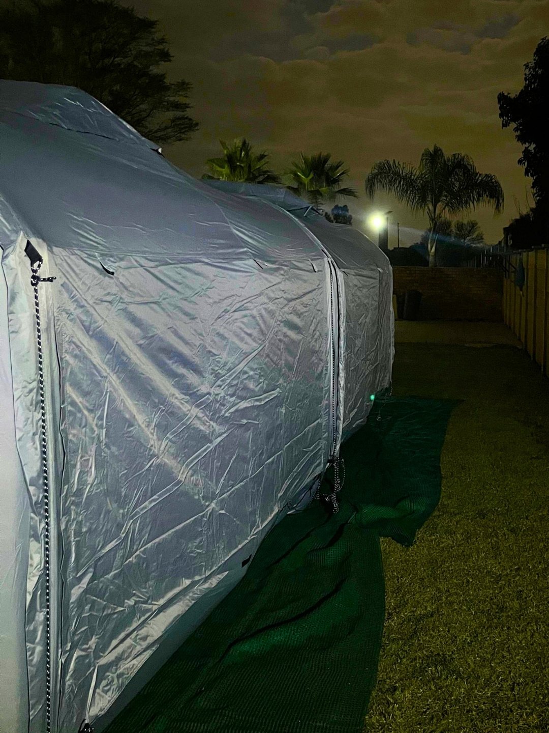The two linked Cube tents at night with the outer rain sheet fitted over the top and guy ropes anchored to the ground
