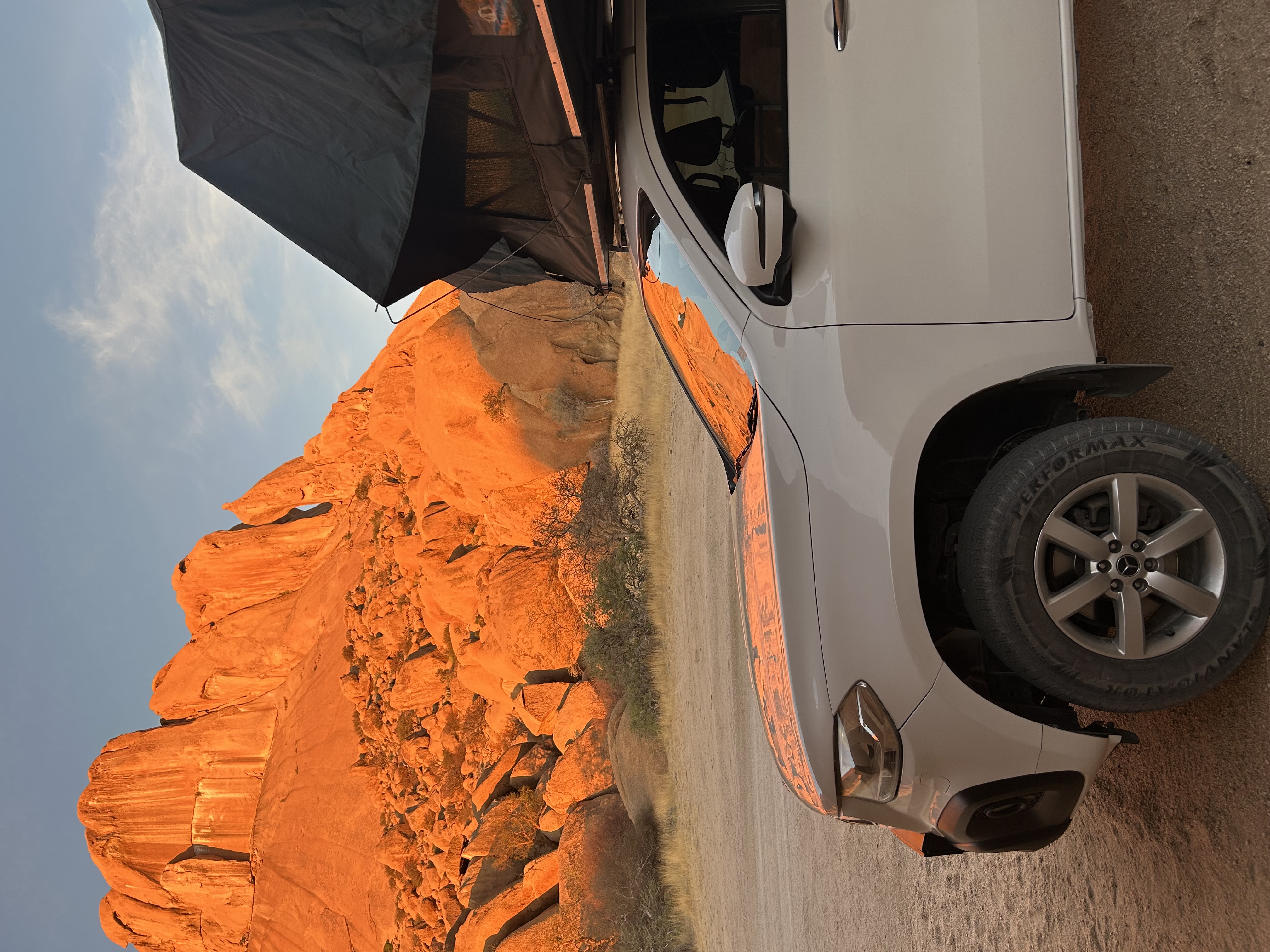 White 4x4 with deployed rooftop tent parked at golden-hour rock formations in South Africa