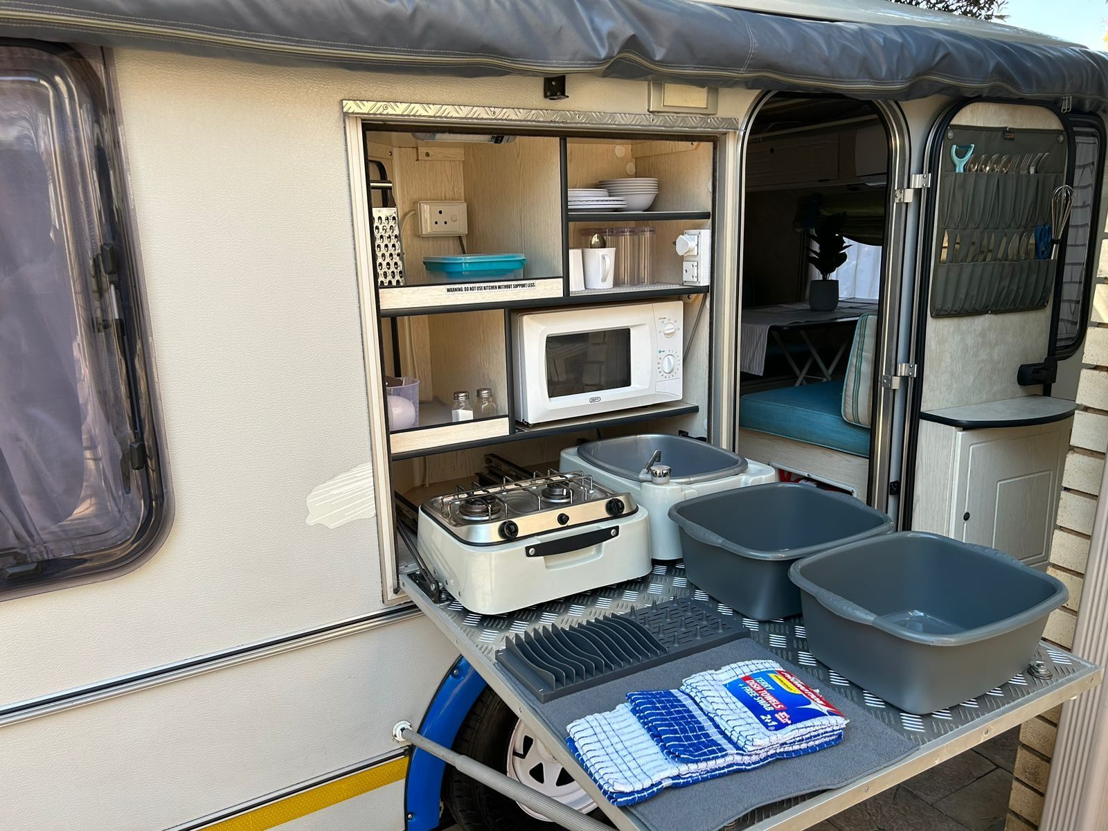 Fully equipped pull-out caravan kitchen with gas stove, microwave and crockery, turning any campsite into a comfortable family base camp