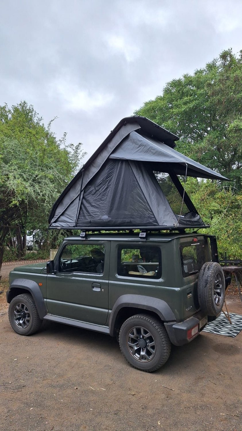 Compact 4x4 with a rooftop tent open at a dry Kalahari style bush campsite