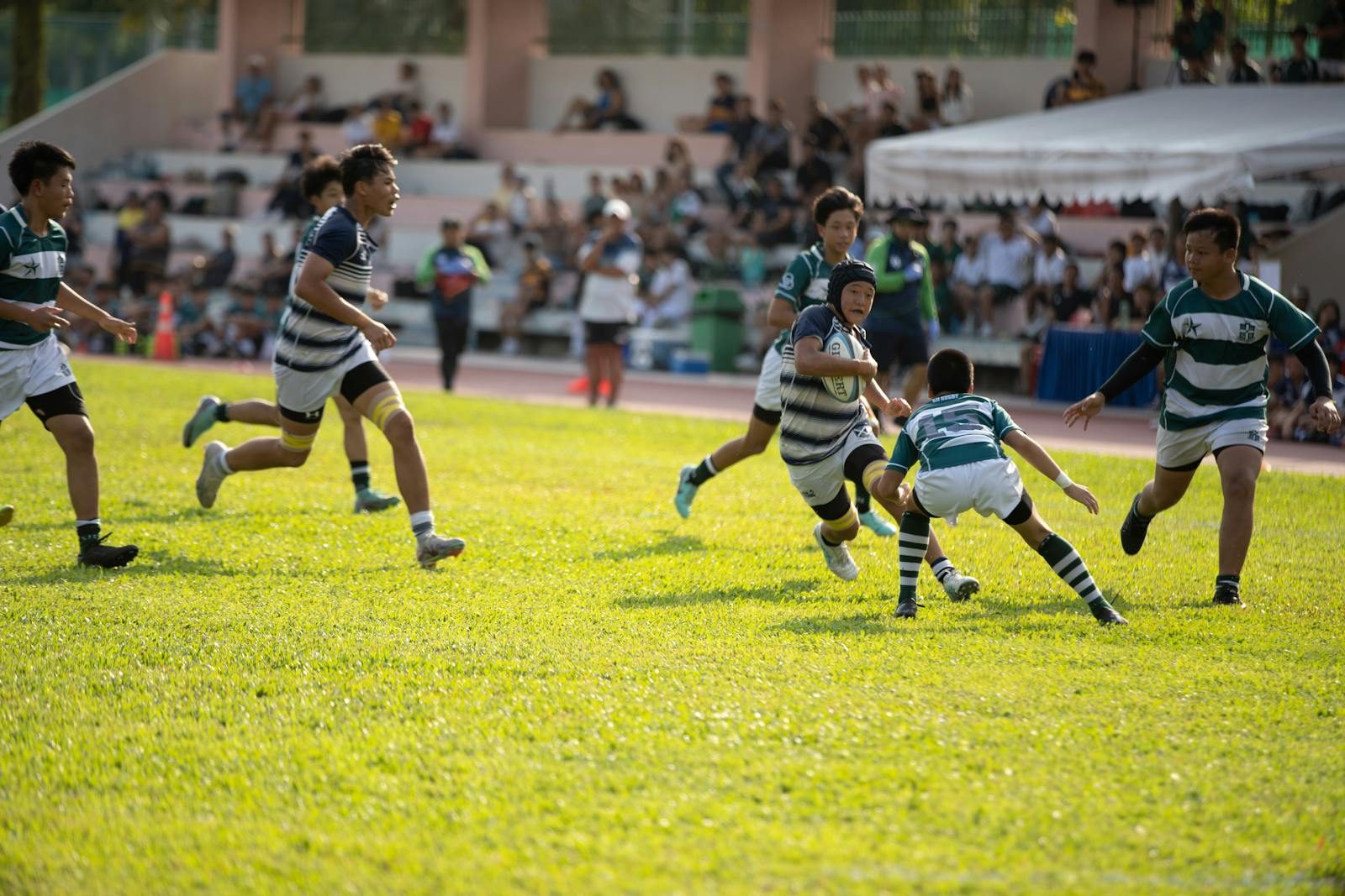 Youth rugby players in action on a sunlit grass field during a school sports tour match