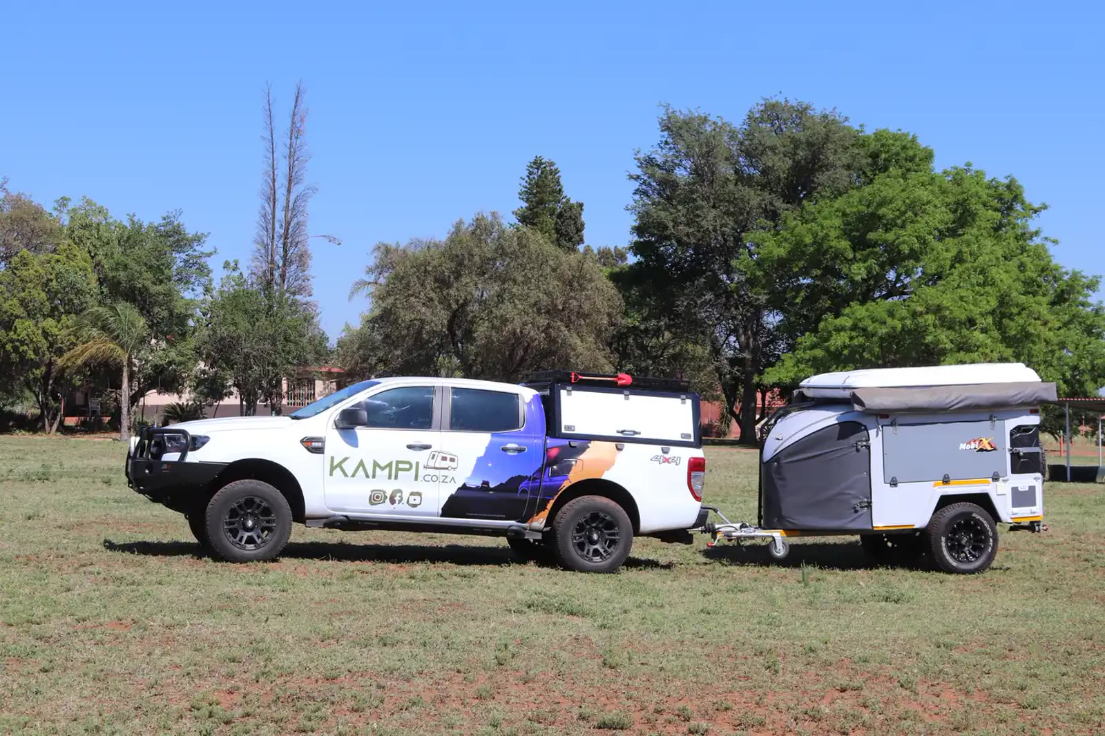 A white Ford Ranger bakkie with a Mobi-X off-road caravan hitched behind it, parked on a grass field