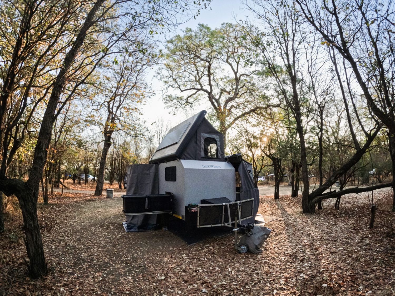 Off-road caravan set up at a quiet winter bushveld campsite with bare trees and a carpet of dry leaves