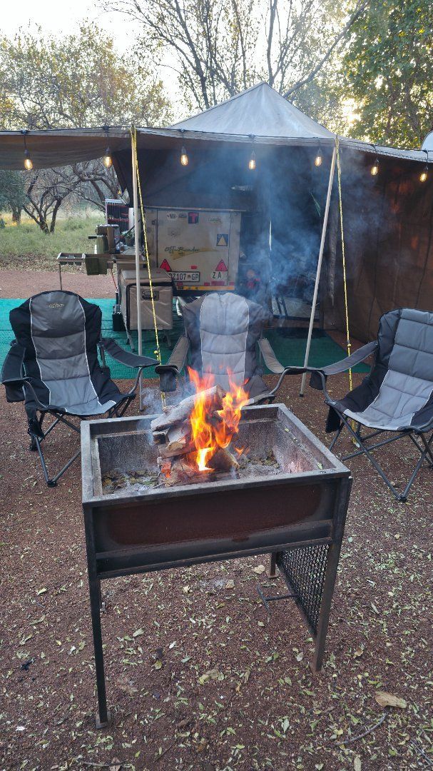 Fire burning in a portable fire pit at dusk with camping chairs arranged around it