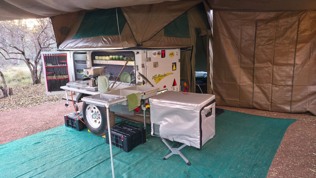Camp kitchen open with a camping fridge on a stand and battery boxes on the ground