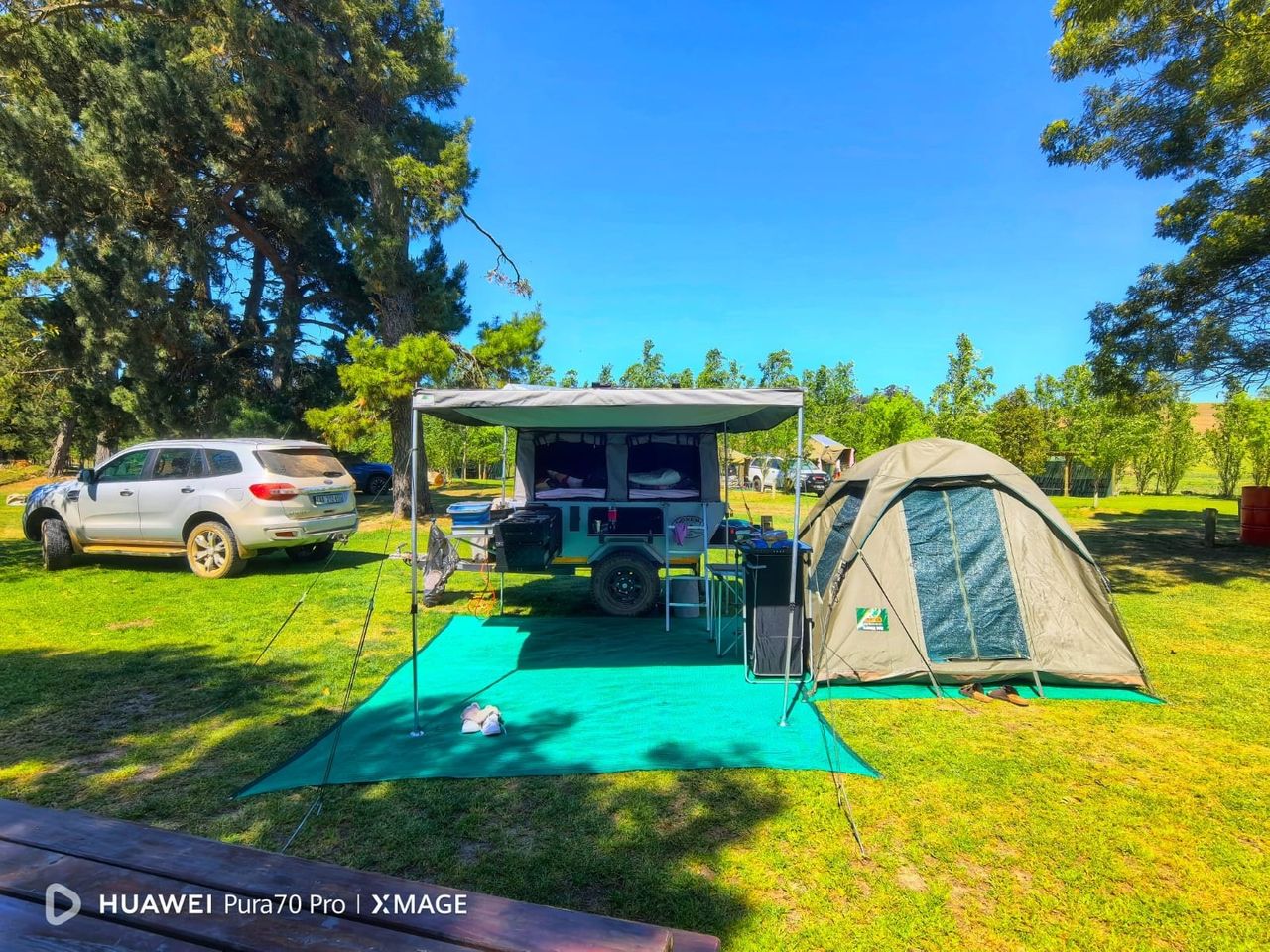 Camping trailer with awning and a separate dome tent pitched alongside on a grassy stand